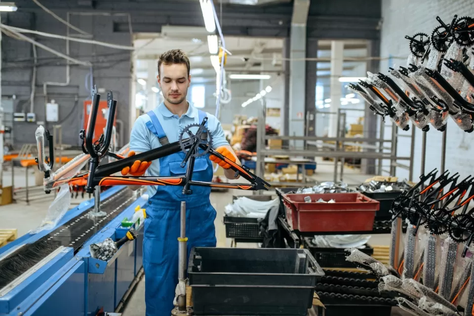Worker in bicycle factory holding black and orange bike frame.